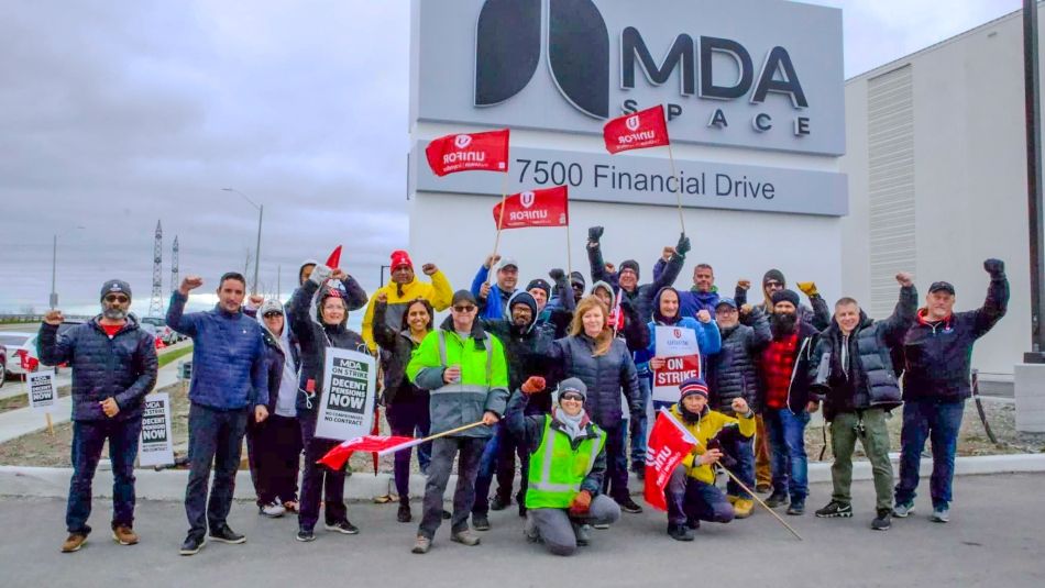 Des travailleurs, le poing levé, se tiennent devant le siège de MDA Space à Brampton, en Ontario.