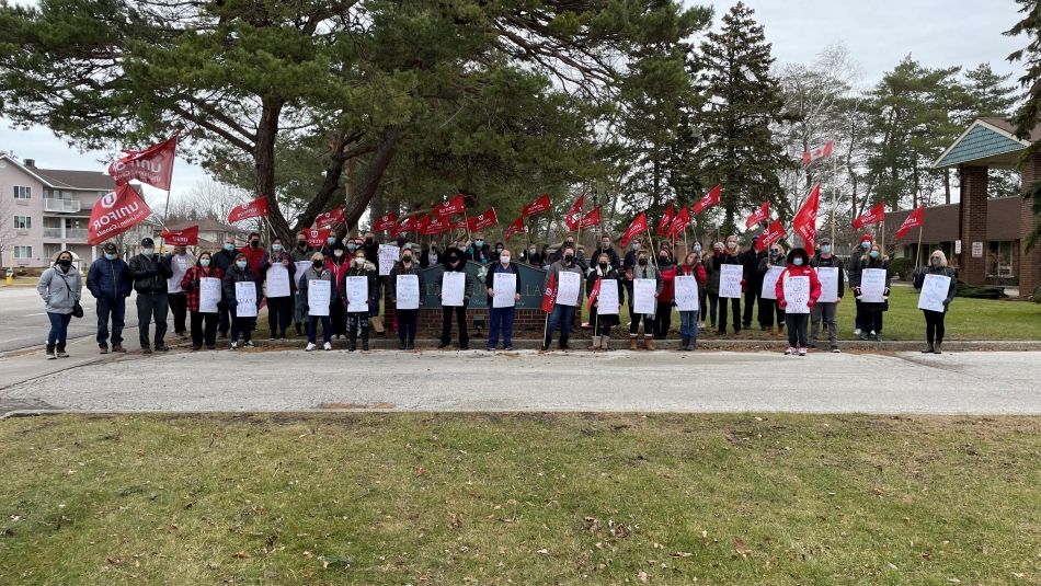 Grand groupe de travailleuses et travailleurs des soins de longue durée debout tenant des pancartes et des drapeaux