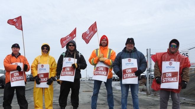 Six people holding on strike place cards and Unifor flags